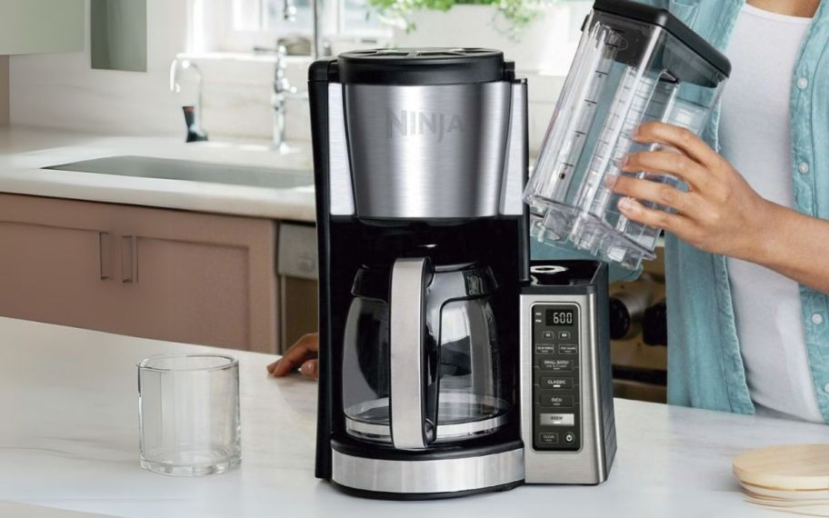 a woman removing the water tank from a ninja coffee maker