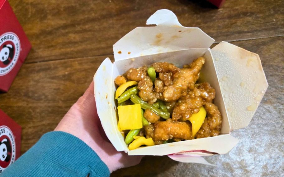a hand holding a container of chinese food