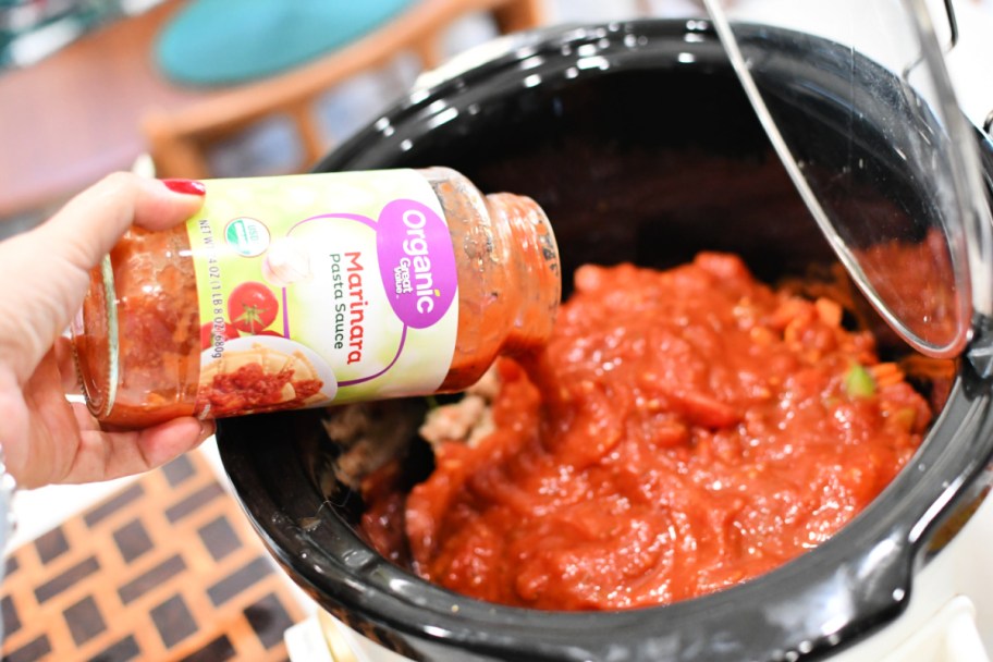 pouring a jar of walmart great value organic marinara into slow cooker 