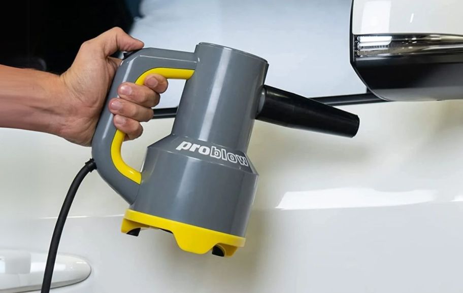 a mans hand holding a handheld blower while drying off a car