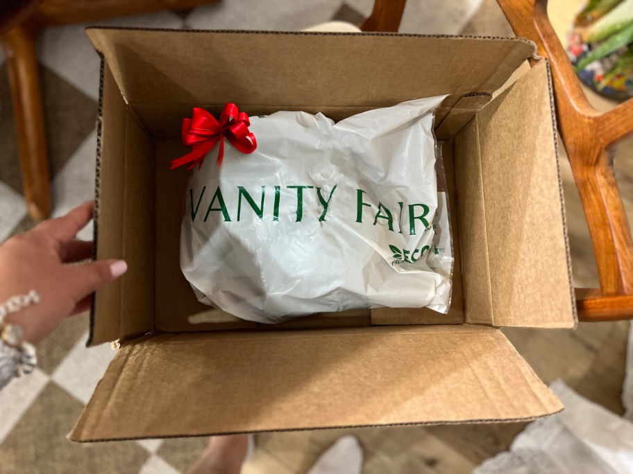 hand lifting a vanity fair package with a bow on it, out of a box