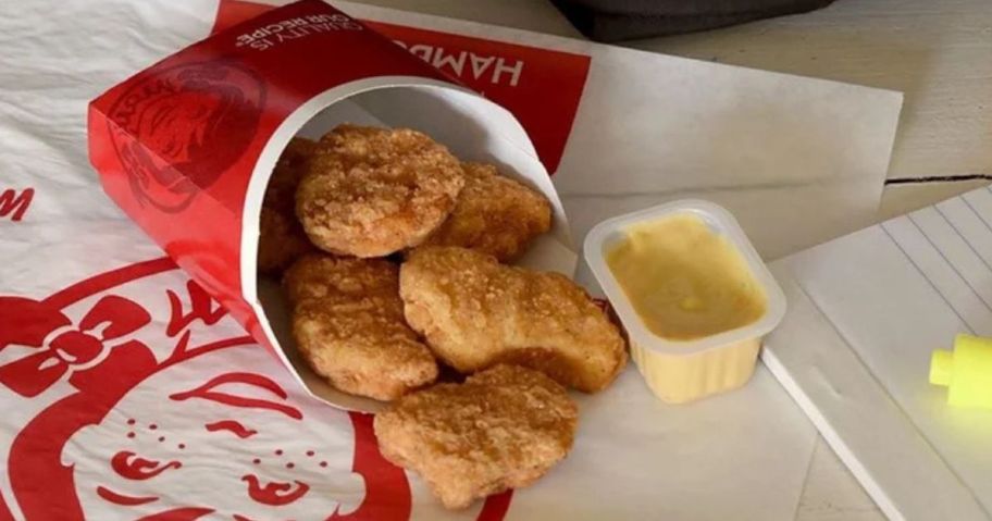 Wendy's chicken nuggets coning out of the container next to a pack of honey mustard sauce on a Wendy's paper wrapper