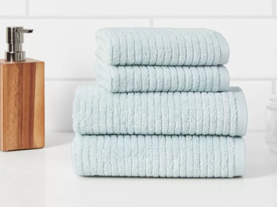 a set of light blue ribbed bath towels and hand towels on a bathroom sink next to a soap pump