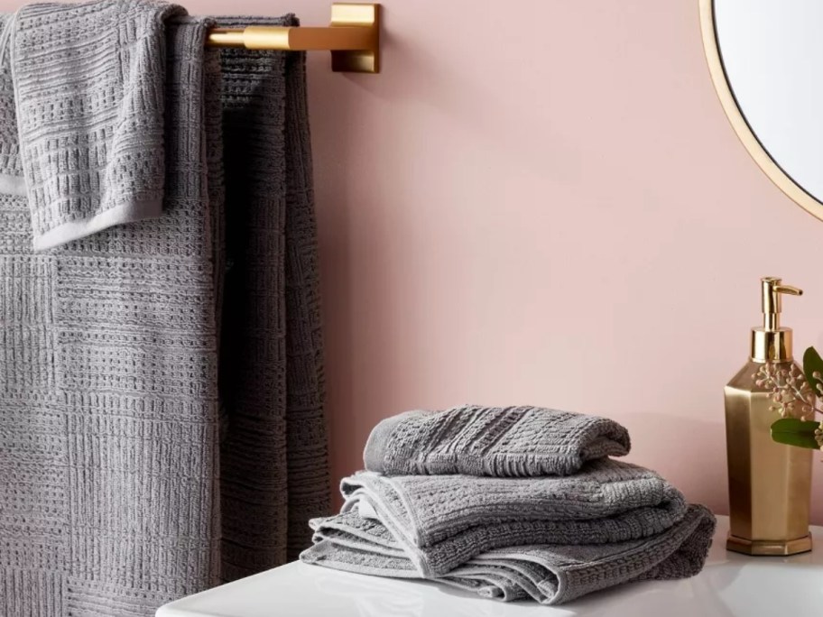 a bathroom with grey hand towels, towels and washcloths on the sink, matching towels hanging on the wall beside it