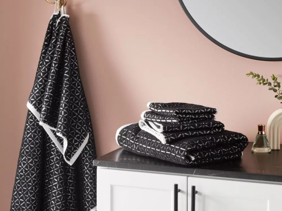 a bathroom with black and white hand towels, towels and washcloths on the sink, matching towels hanging on the wall beside it