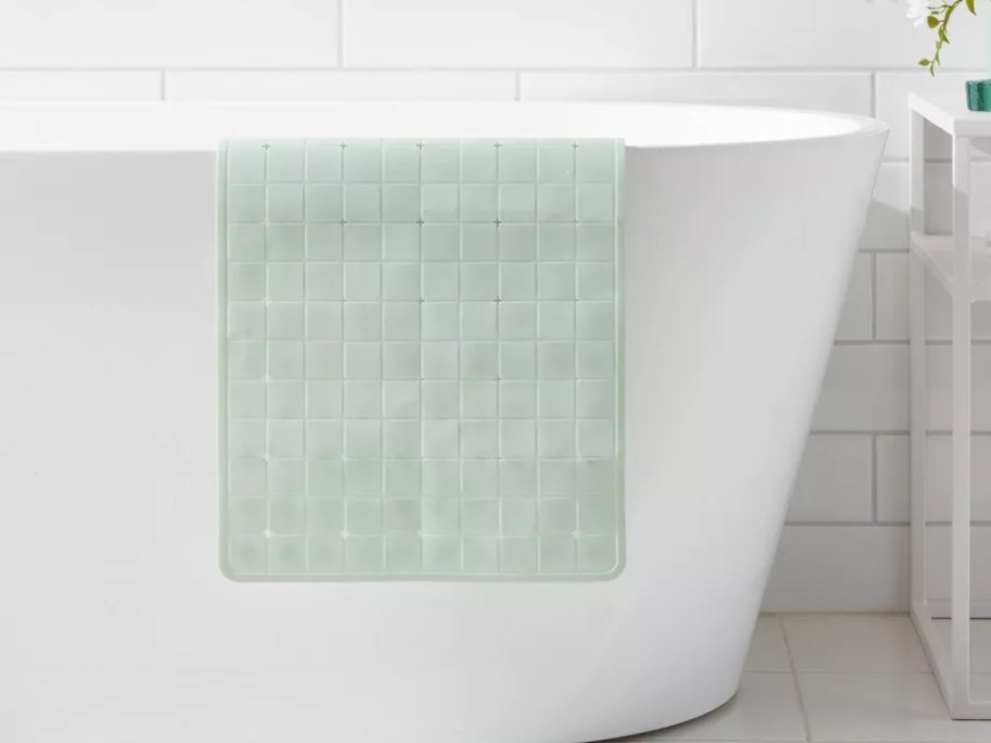 a light min green bathmat hanging over the side of a white bath rub