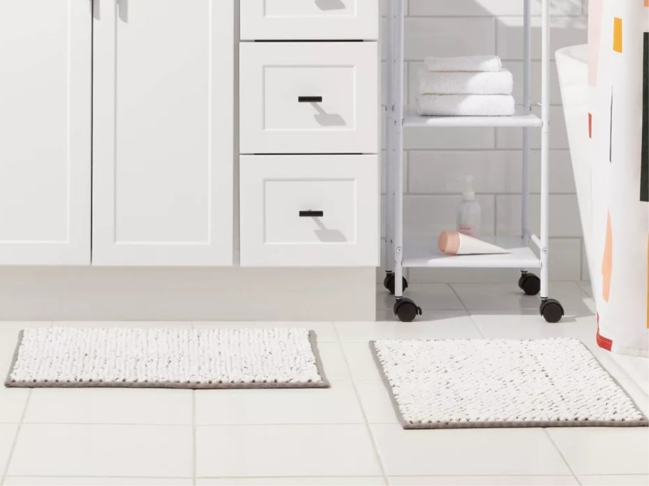 two white and grey bath rugs on a white tile bathroom floor