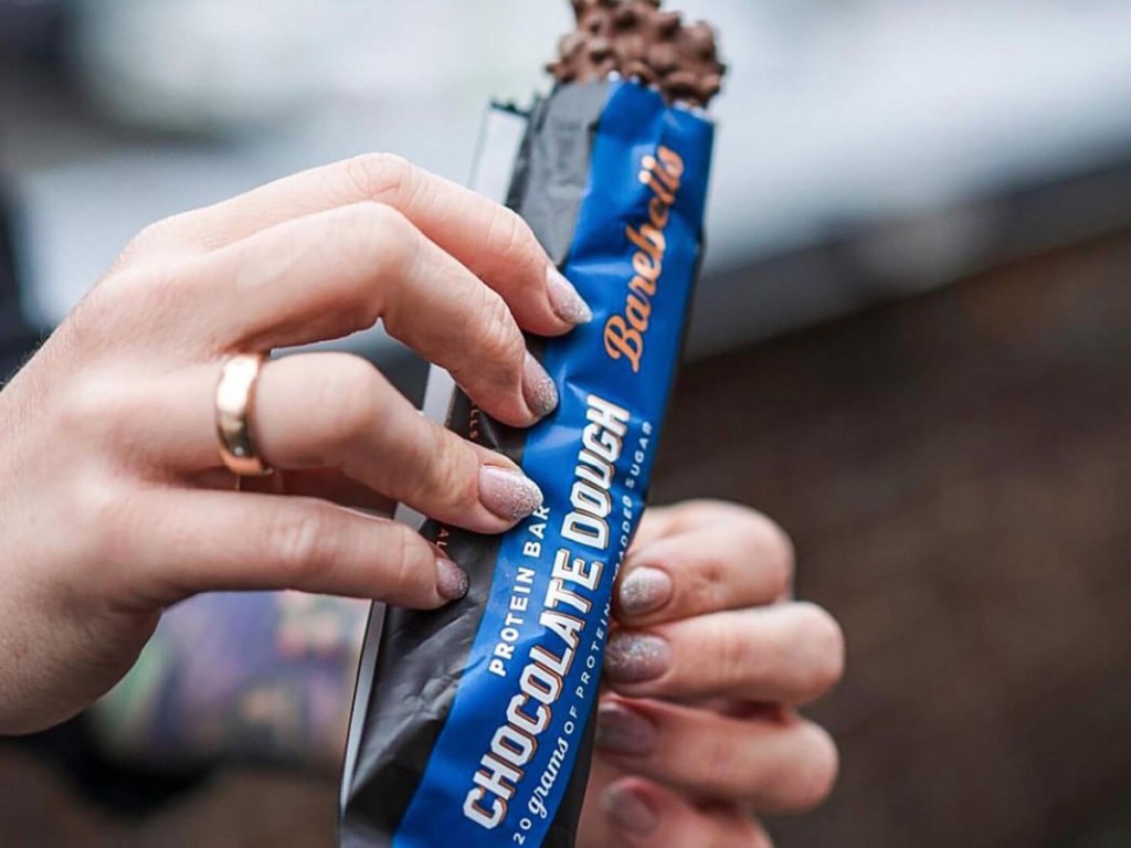 Person holding opened barbells, chocolate dough, protein bar