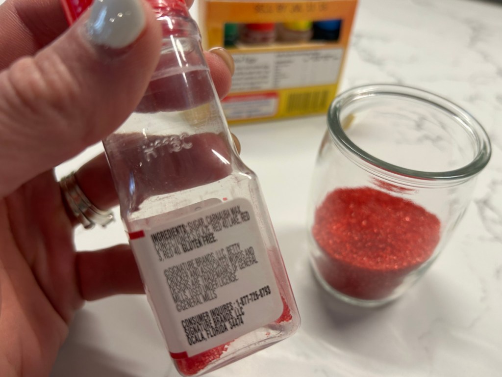 Person holding bottle of Betty Crocker red colored sprinkles, showing off the ingredients