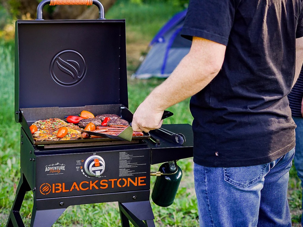 Person wearing blue jeans, cooking on Blackstone grill outside