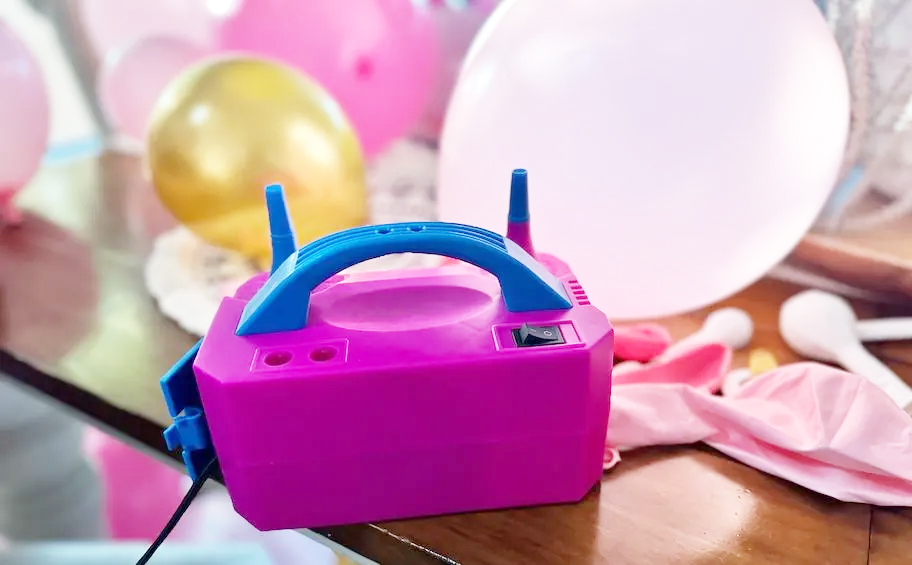 pink and blue balloon pump on floor in front of gold balloons