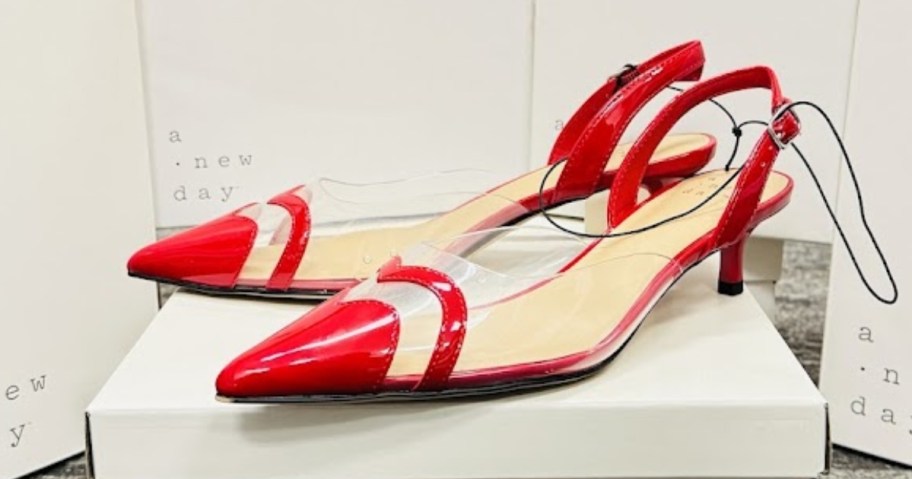 a pair of women's 2 inch high heel shoes in red and clear sitting on a white shoe box with more white shoe boxes behind it