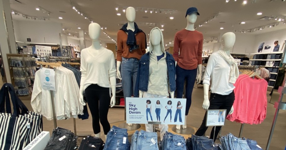 the front display in a GAP Factory store with mannequins wearing shirts, jeans, jackets, and more jeans on a table in front of them