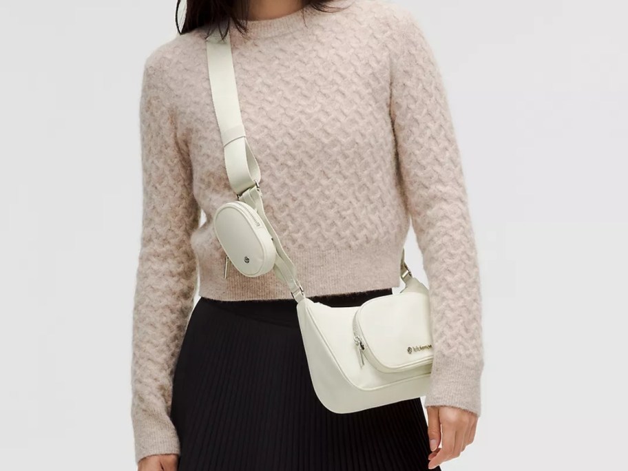 woman in a light tan sweater and brown pants wearing a cream color crossbody bag