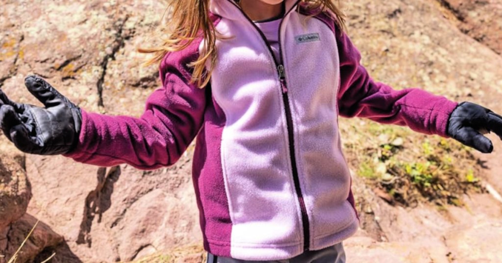 Little girl, wearing purple and pink, zip up Columbia, fleece jacket and standing in front of rock Canyon