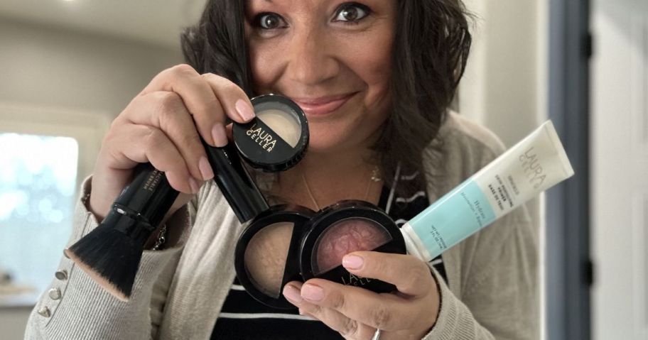 Woman holding many laura geller beauty products