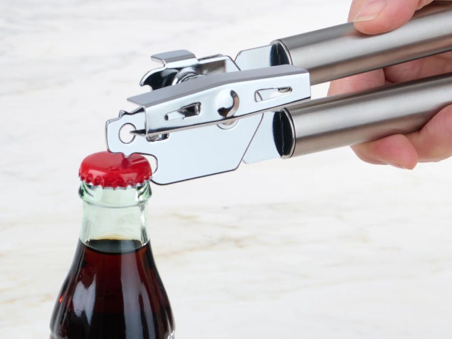 hand using a mainstays can opener to remove the top from a glass bottle of cola