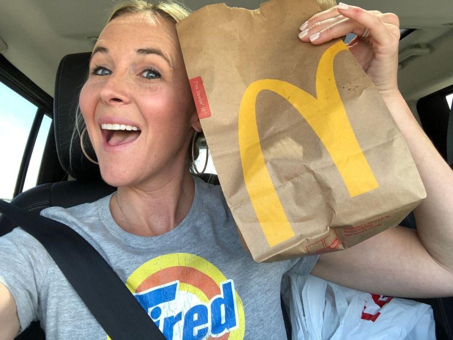 Woman smiling and holding up a McDonald's bag while in her car