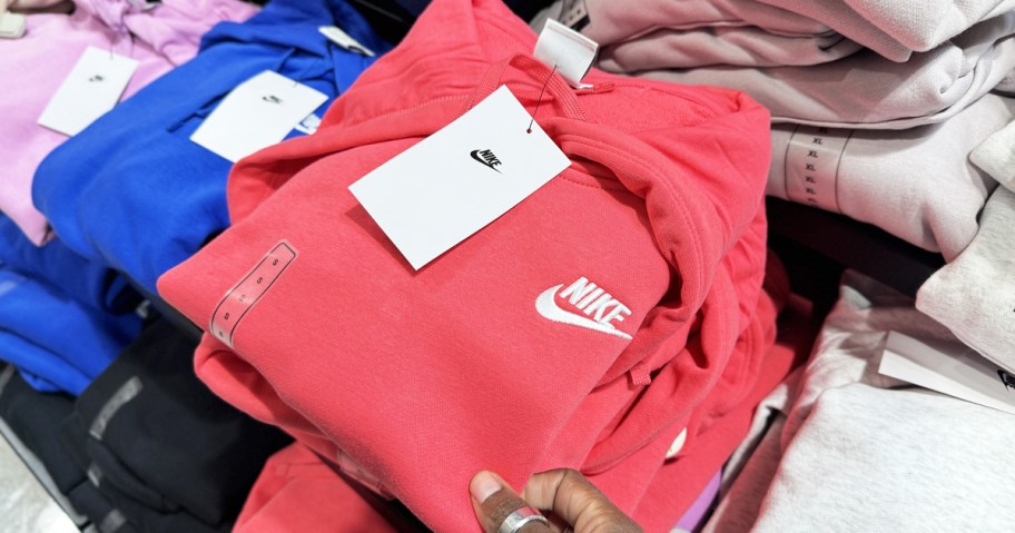 hand touching a bright pink folded nike hoodie in store