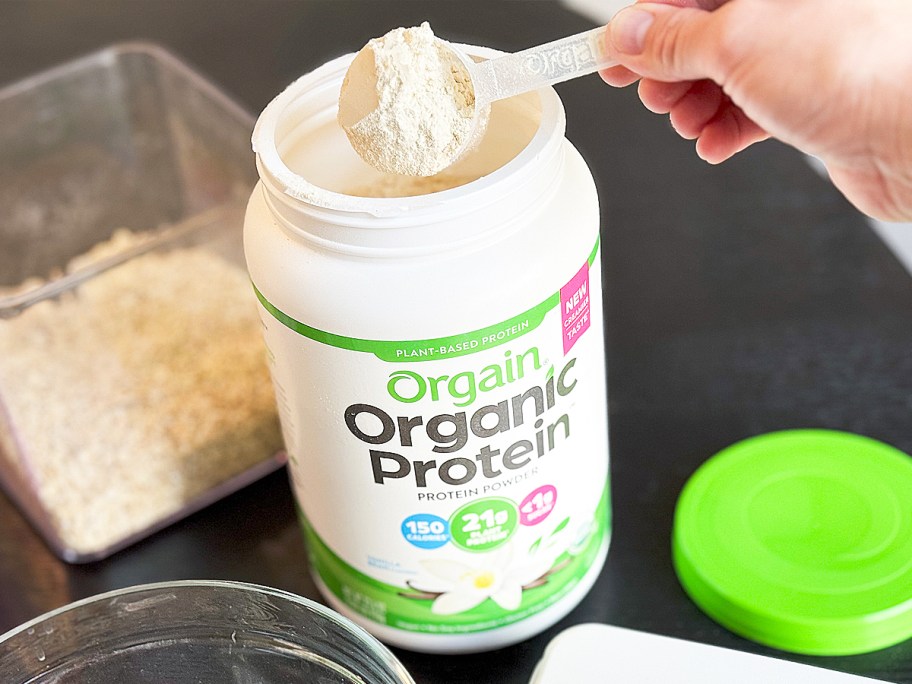 hand taking a scoop out of a jar of Orgain Organic Vegan Vanilla Bean Protein Powder