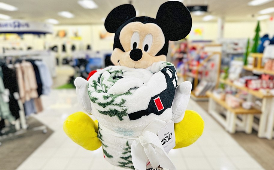 hand holding up a Mickey Mouse plush and throw blanket set in store