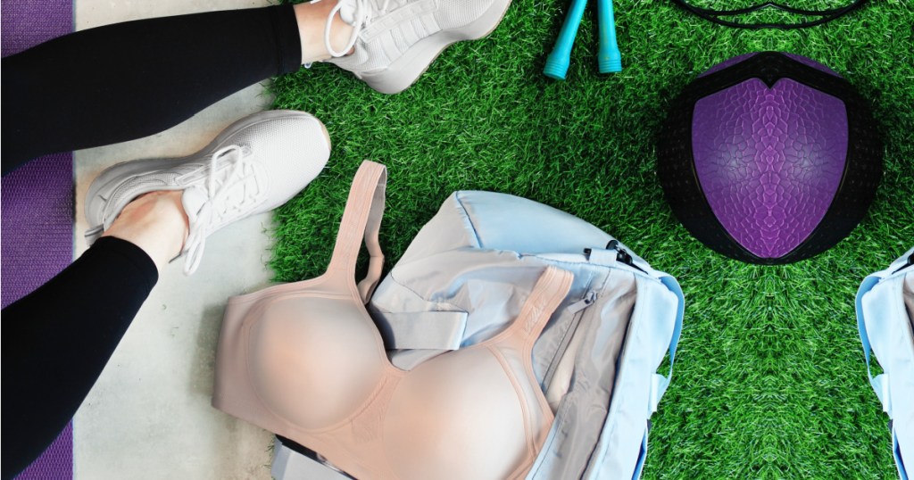 Pink sports bra on top of gym bag next to person sitting in grass by ball and jump rope