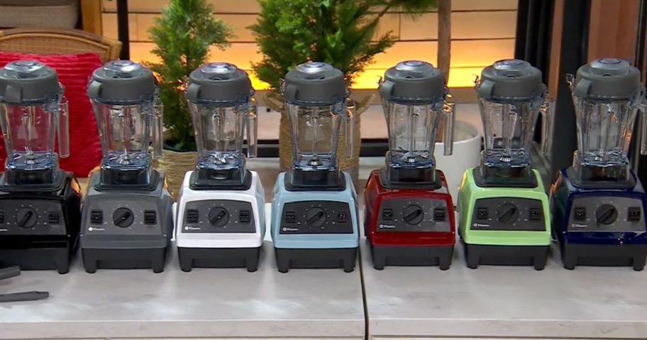 Seven Vitamix Blenders in different colors lined up on a counter