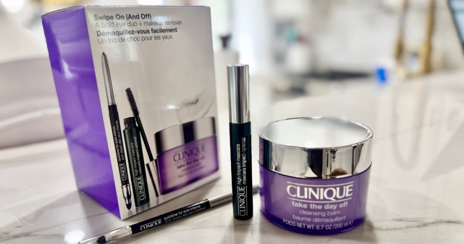 a box picturing Clinique items next to a Clinique Mascara, eye liner and large container of makeup remover on a granite countertop