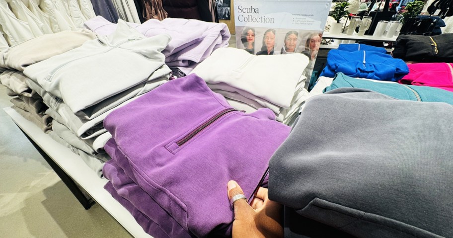 hand touching a folded purple half-zip sweatshirt on store display table