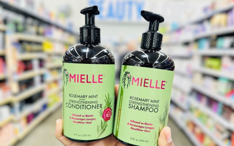 a womand hand holding a bottle of shampoo and a bottle of conditioner in a store on an aisle