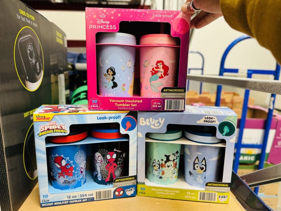 a womans hand reaching for a 2 pack of kids character tumblers