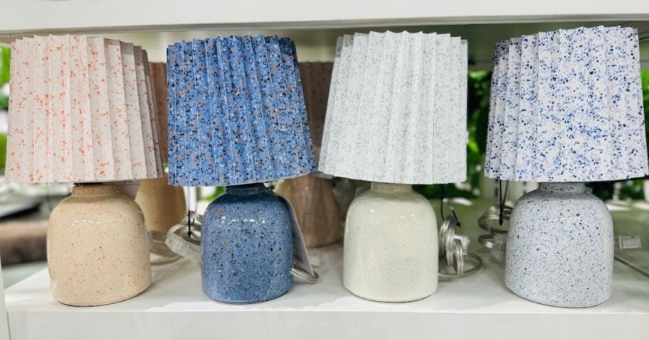 4 table lamps in soft pastel color with pleated shades on a store display shelf