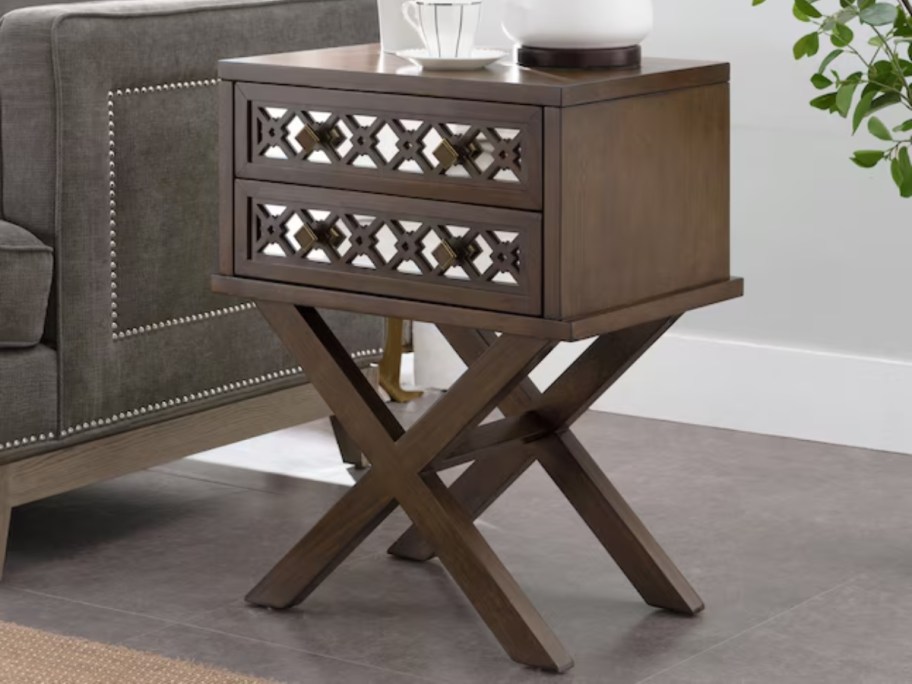 a dark brown nightstand with X shaped legs and a silver mirror inlay on the 2 drawers