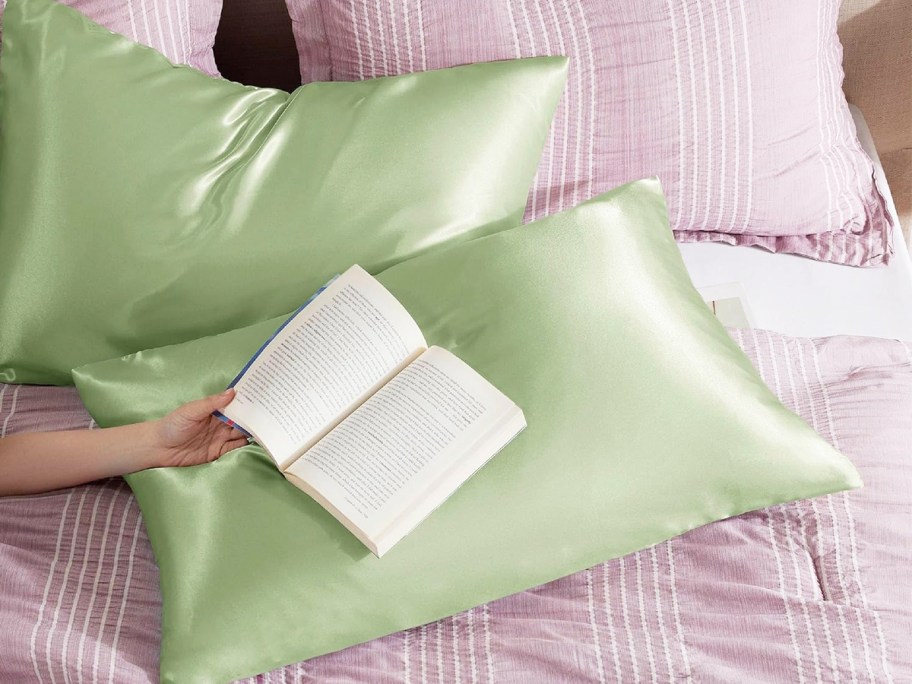 person holding a book over a set of green satin pillowcases