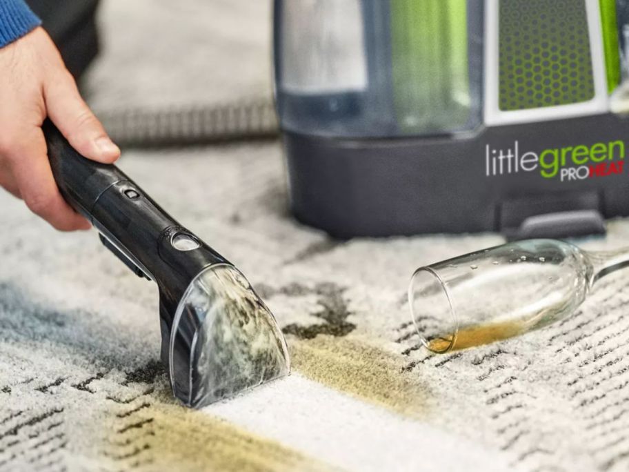 A person using a Bissell Little Green Premier Pet Deep Cleaner to clean a spilled drink on a carpet