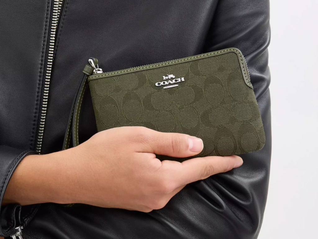 Person holding olive colored coach wristlet while wearing black leather jacket