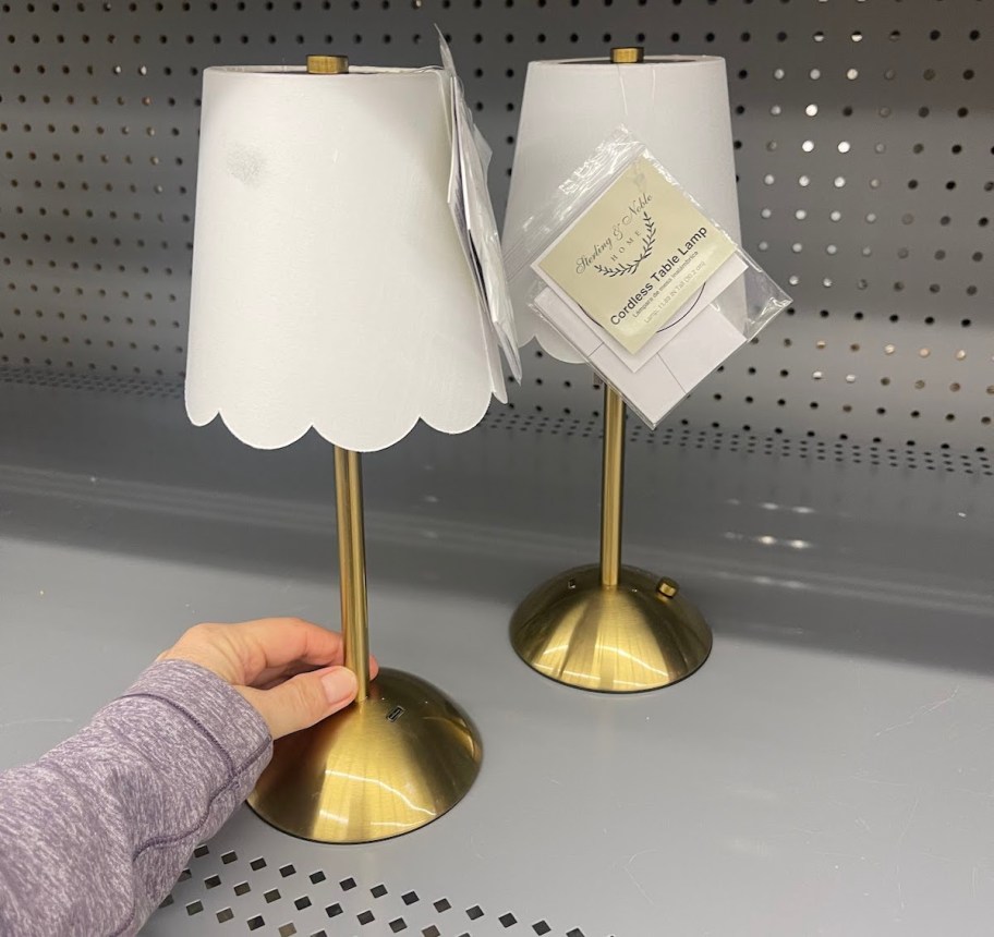 hand holding bottom of brass and white scalloped lamp on store shelf