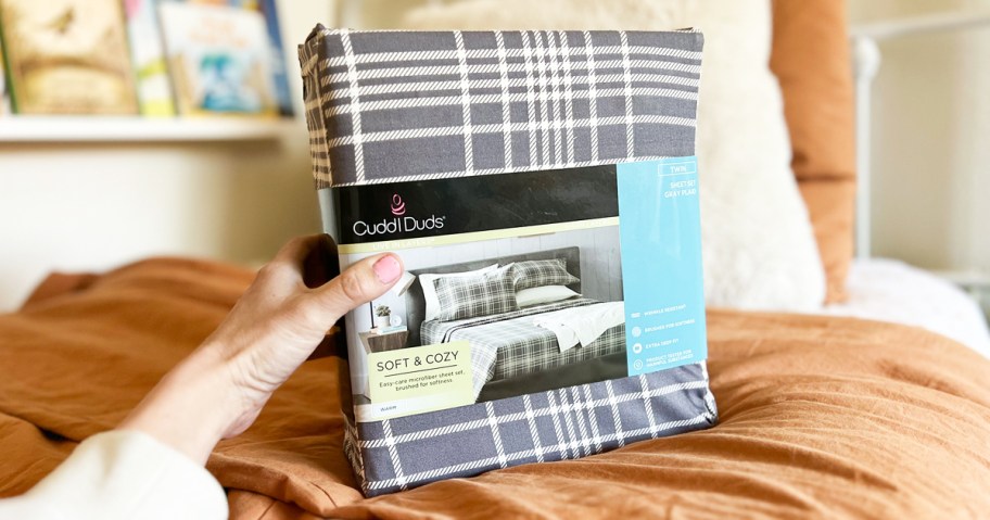 hand holding a grey plaid set of Cuddl Duds Sheets on bed