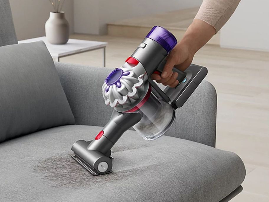 A person using a Dyson handheld vac on a couch 