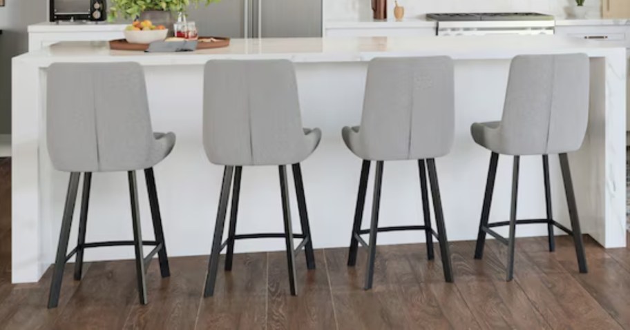 a set of 4 grey upholstered bar stools at a white kitchen bar counter