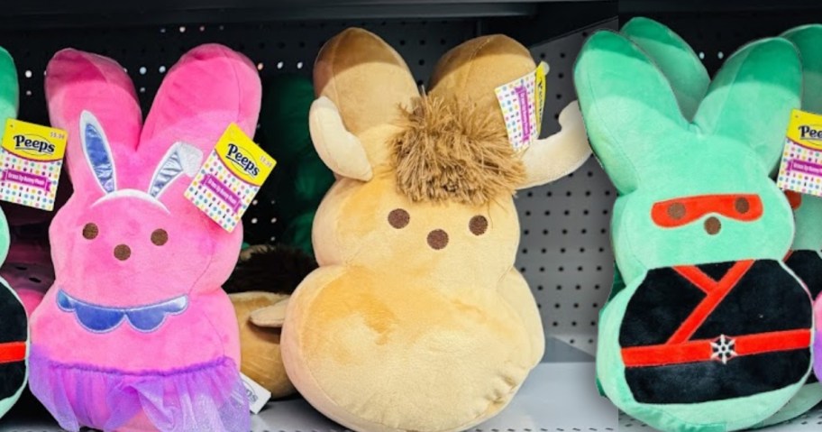 3 plush Peeps bunnies on a Walmart store shelf, one is green and dressed in black and red Ninja gear, one is pink and dressed in purple ballerina outfit, and one is tan and has horns and a tuft of hair so he looks like a Buffalo