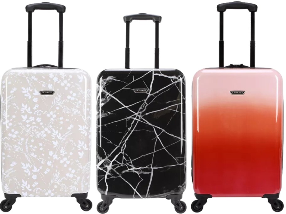 3 carry on size hard sided spinner luggage pieces, one is tan with white flowers, one is black with white designs, and one ia pink and orange ombre