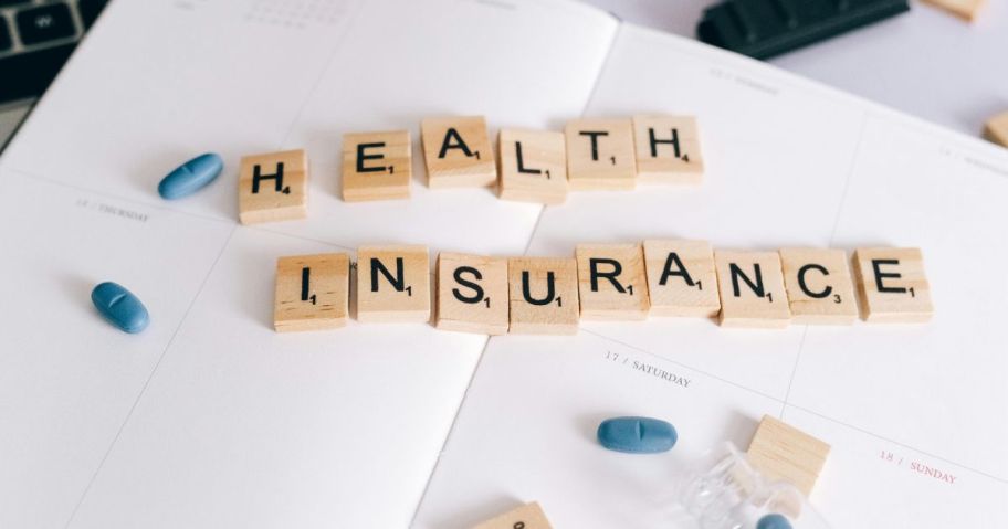 A calendar with scrabble tiles spelling the words health insurance surrounded by blue pills