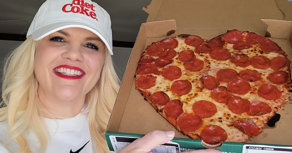 Woman wearing Diet Coke hat, holding pizza box with heart shaped pizza