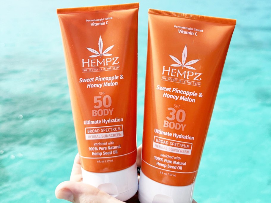 hand holding two orange bottles of Hempz Daily Body Sunscreen