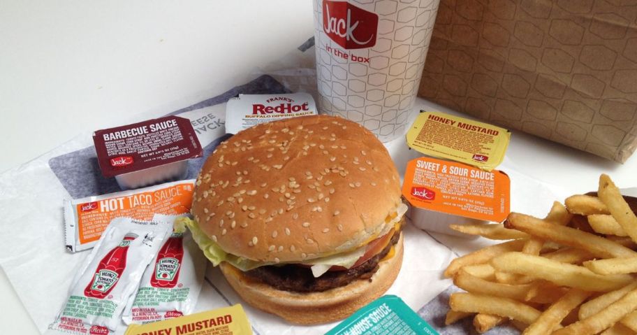 Jack in the box burger next to a soda, fries and different packets of sauce