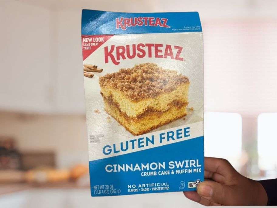 Krusteaz Gluten-Free Cinnamon Swirl Crumb Cake & Muffin Mix 20oz Box in hand in kitchen