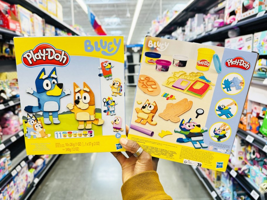 holding up two boxes of Play-Doh Bluey Make 'n Mash Costumes Playsets in store