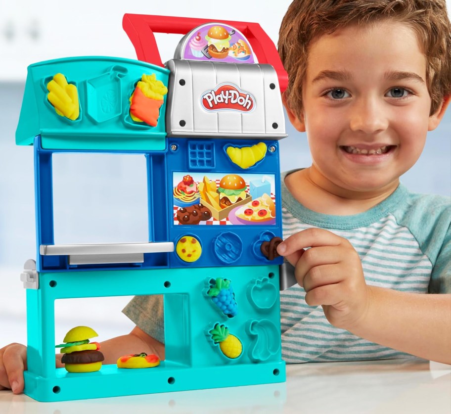 boy next to Play-Doh Kitchen Creations Busy Chef's Restaurant Playset