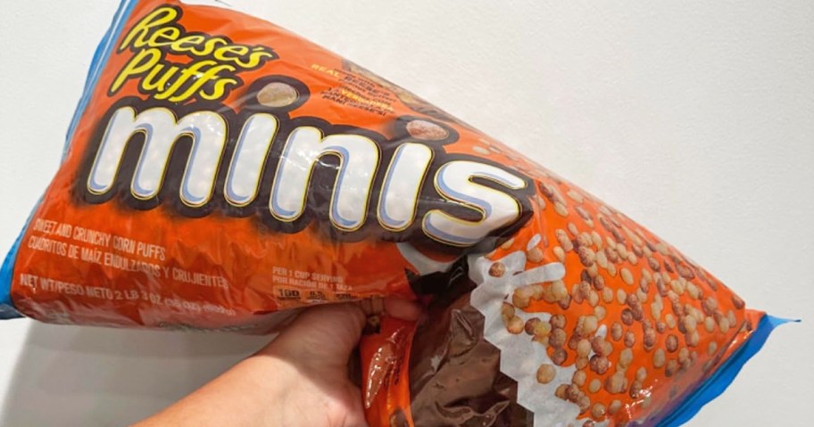 hand holding up a large orange bag of Reese's Puffs Minis cereal
